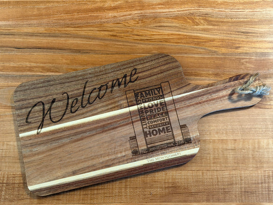 Acacia wood cutting board engraved with the words "Welcome" or "Welcome Home" accompanied by an outline sketch of the recipient's home or apartment/condo building.