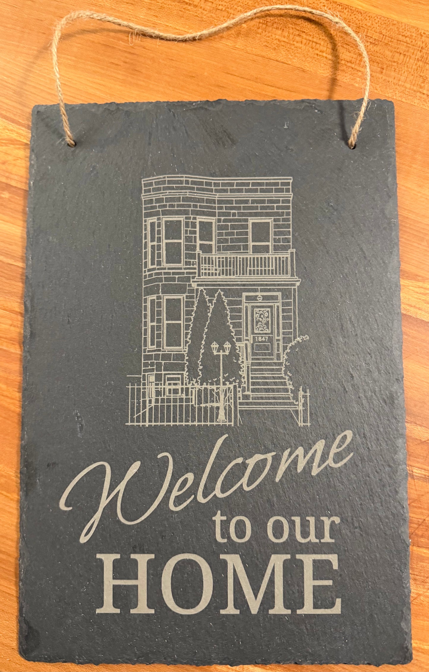 Portrait-oriented slate sign engraved with the words "Welcome to our home" accompanied by an outline image of the recipient's home or condo/apartment building.