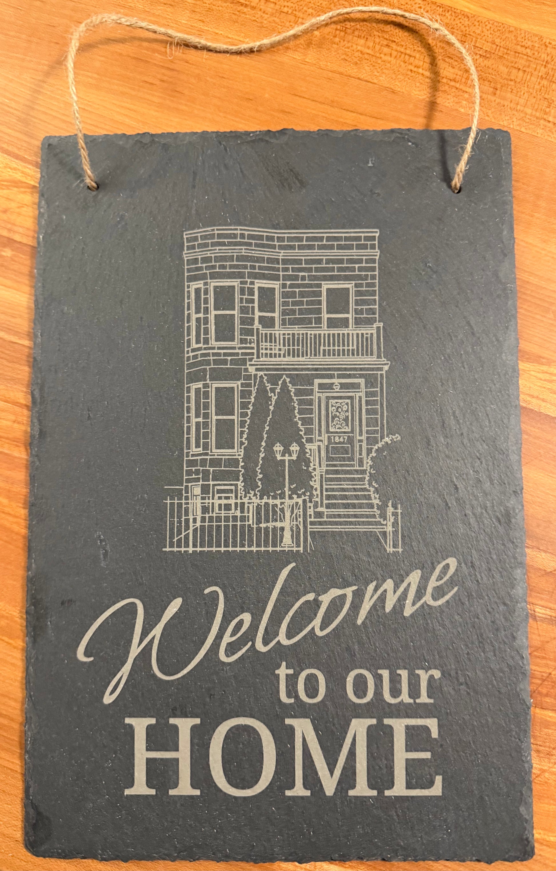 Portrait-oriented slate sign engraved with the words "Welcome to our home" accompanied by an outline image of the recipient's home or condo/apartment building.