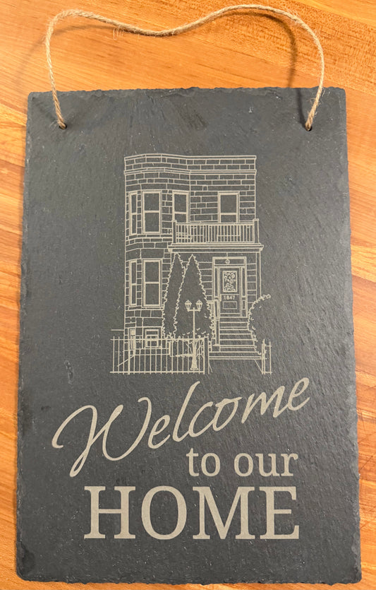 Portrait-oriented slate sign engraved with the words "Welcome to our home" accompanied by an outline image of the recipient's home or condo/apartment building.